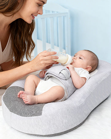 Caregiver bottle-feeding a baby with the support pillow